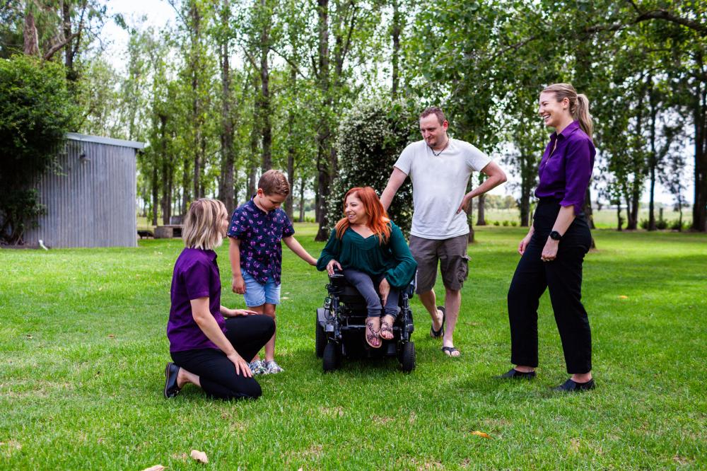 A family is sitting around a participant in a wheelchair as she speak to her OR